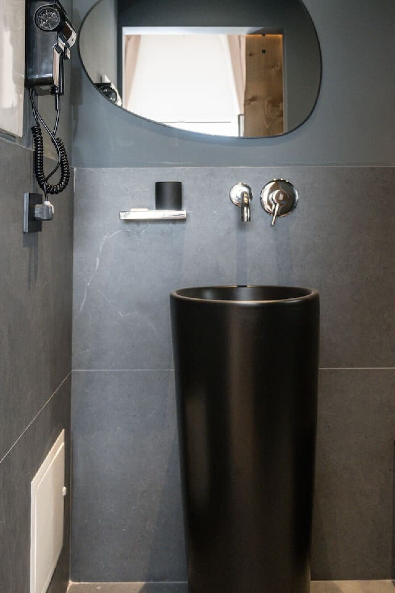 A bathroom with a large black sink, a mirror, and a hairdryer mounted on the wall.
