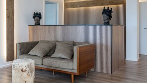 Een moderne woonkamer met een grijze bank, een houten salontafel en een decoratief wandpaneel.
