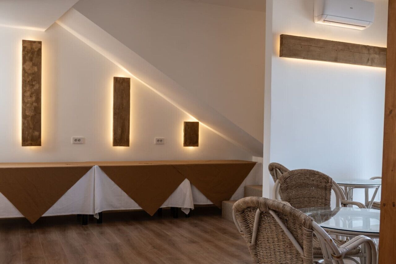 Et moderne spiseområde med et langt bord, stole og vægmonteret belysning.