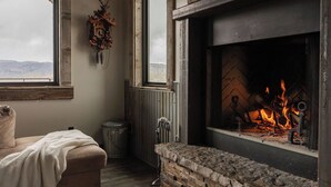 A cozy room with a fireplace, a window with a view of the mountains, a radiator, and a bench with a blanket. - Modern Cabin at Blue Mesa, INCREDIBLE VIEWS, 40min from BLK CNYN (Gunnison)