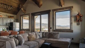 A spacious living room with a large sectional sofa, a cowhide rug, and a view of mountains through large windows. - Modern Cabin at Blue Mesa, INCREDIBLE VIEWS, 40min from BLK CNYN (Gunnison)