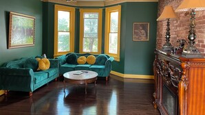 A room with a green wall, a green sofa set, a round coffee table, and a fireplace with decorative items. - Step back in time and experience the elegance of Victorian era.  (Reading)