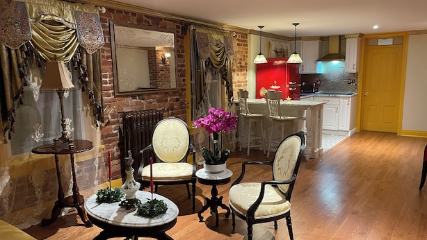 A living room with a fireplace, a dining area with a table and chairs, and a kitchen area with a red island and modern appliances. - Step back in time and experience the elegance of Victorian era.  (Reading)