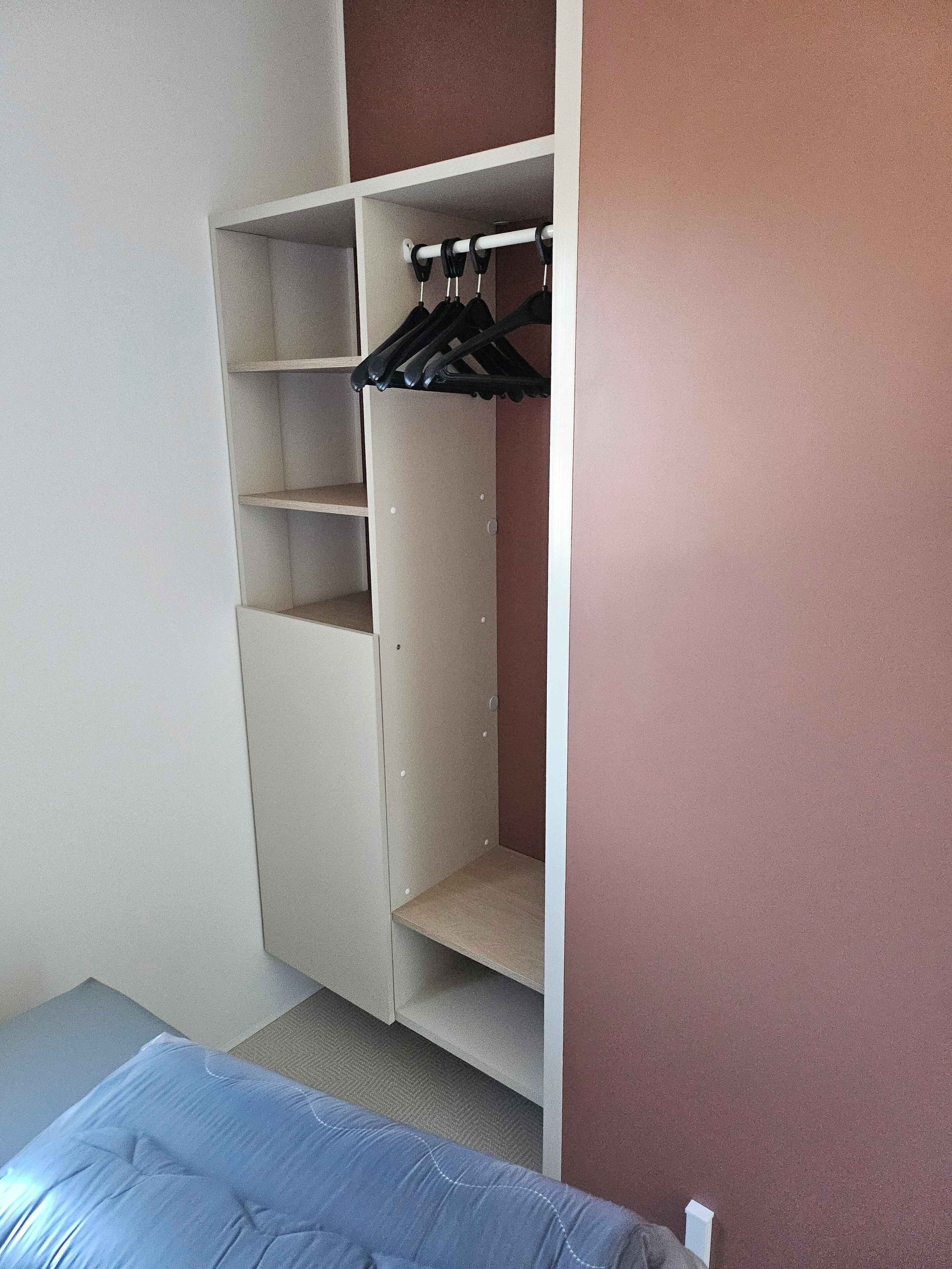 A bedroom with a bed, a wardrobe with multiple shelves, and a hanging closet rod.
