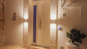 L’entrée d’un hôtel, avec un mur en pierre, une porte ornée d’une bande violette et un pot de fleurs.