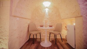 Une pièce accueillante, à l’architecture arrondie, avec une table ronde et deux chaises, un petit réfrigérateur blanc et un luminaire au plafond.