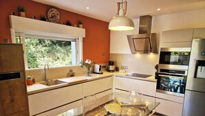 A modern kitchen with a glass dining table, stainless steel appliances, and a window overlooking greenery.
