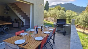 An outdoor dining area with a wooden table set for four, a barbecue grill, and a staircase leading to an upper level.