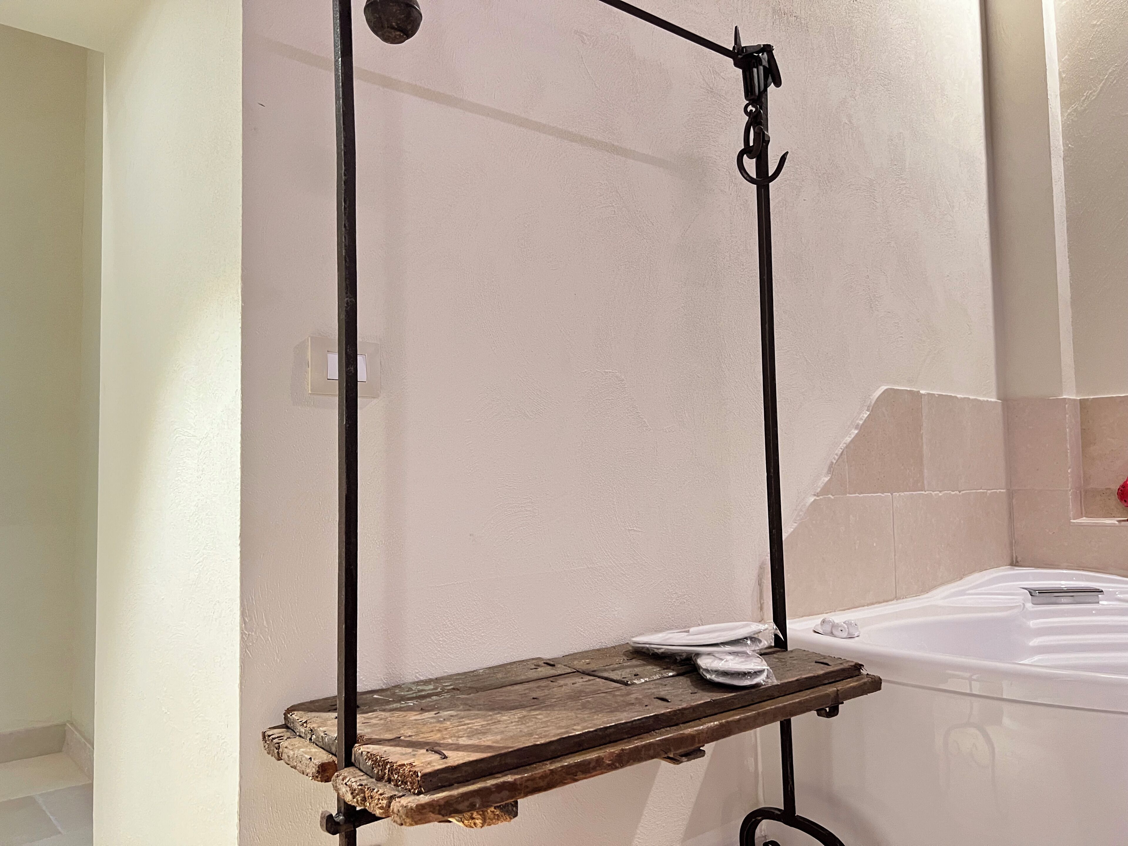 Un baño con un estante de madera, una bañera blanca y un perchero para toallas.