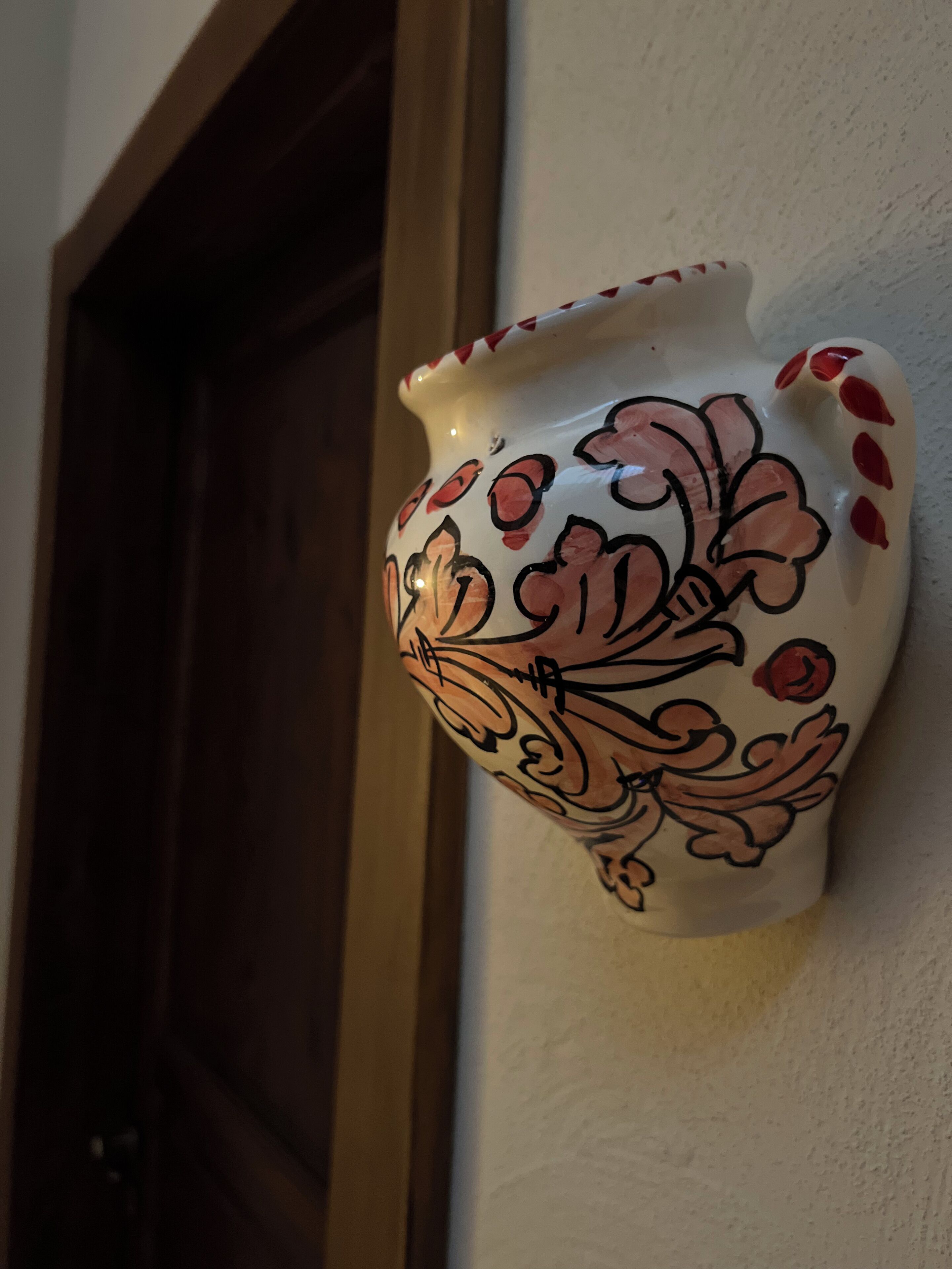 A ceramic vase with floral patterns and red accents, mounted on a wall.