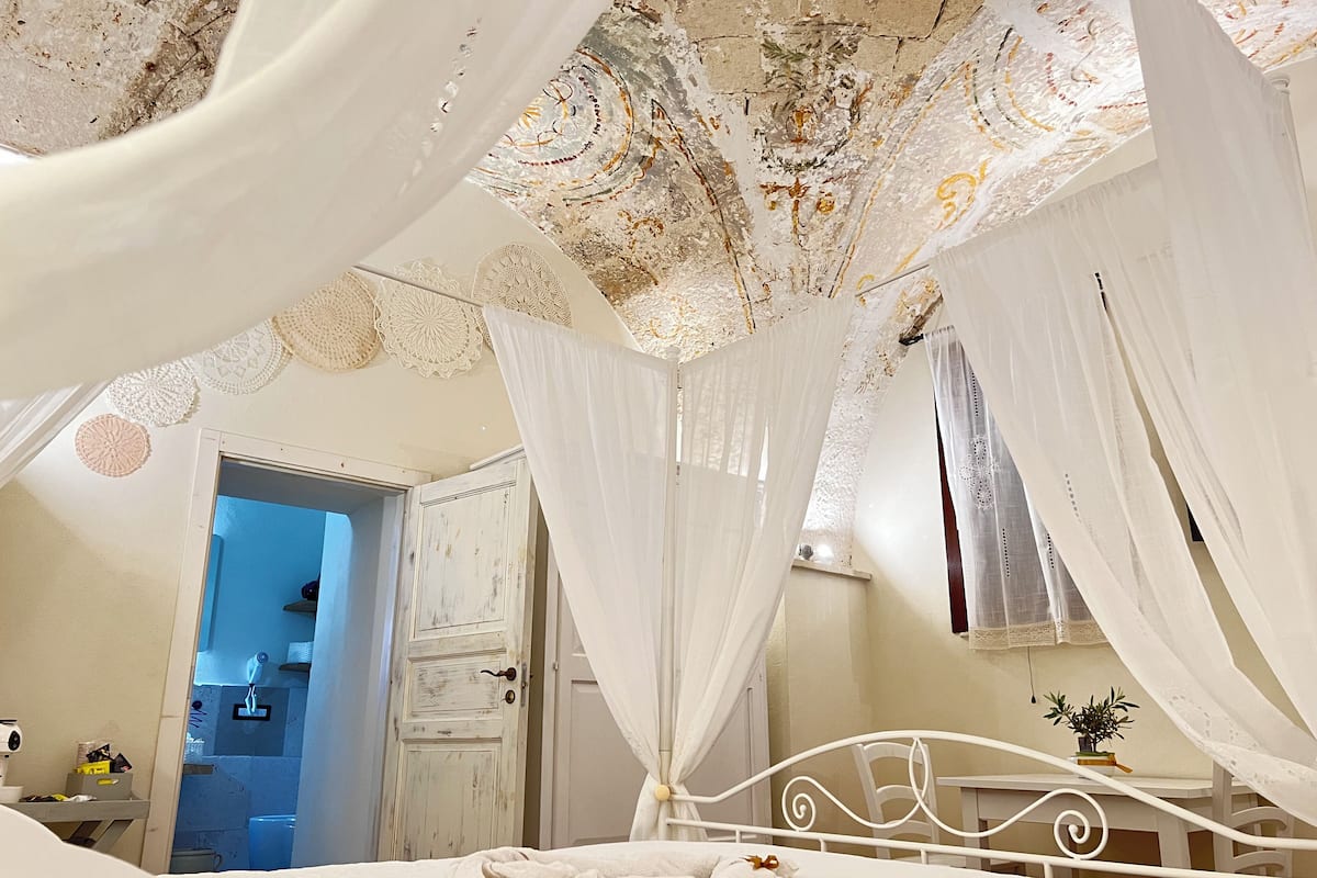 Une chambre à coucher avec un lit, des rideaux blancs et un plafond orné d’un motif floral.