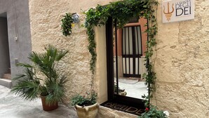 Entrada de un edificio con un letrero que dice "La Dimora Dei", una planta en maceta y una puerta con un portón negro.