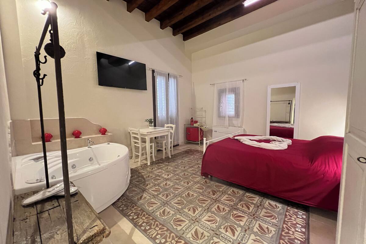 Une chambre avec un grand lit, une petite table avec des chaises, un téléviseur fixé au mur et une baignoire.