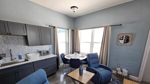 Une cuisine moderne avec des meubles gris, un plan de travail blanc et un four encastré. On y trouve également un coin repas avec une table ronde, des chaises bleues et un petit tapis.