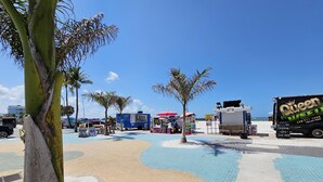 Une zone aménagée au bord de la plage, avec des palmiers, un camion-restaurant et un véhicule portant l’inscription « Queen Weed ».