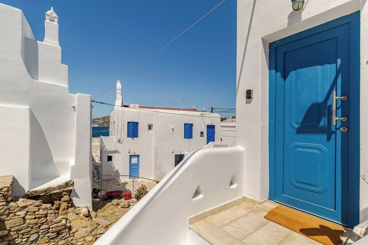 A white building with a blue door, a stone wall, and a clear blue sky.