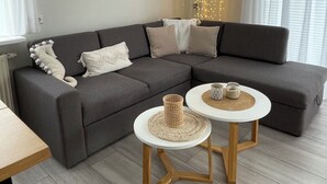 Un salon moderne avec un canapé d’angle gris, deux petites tables rondes et un luminaire décoratif.