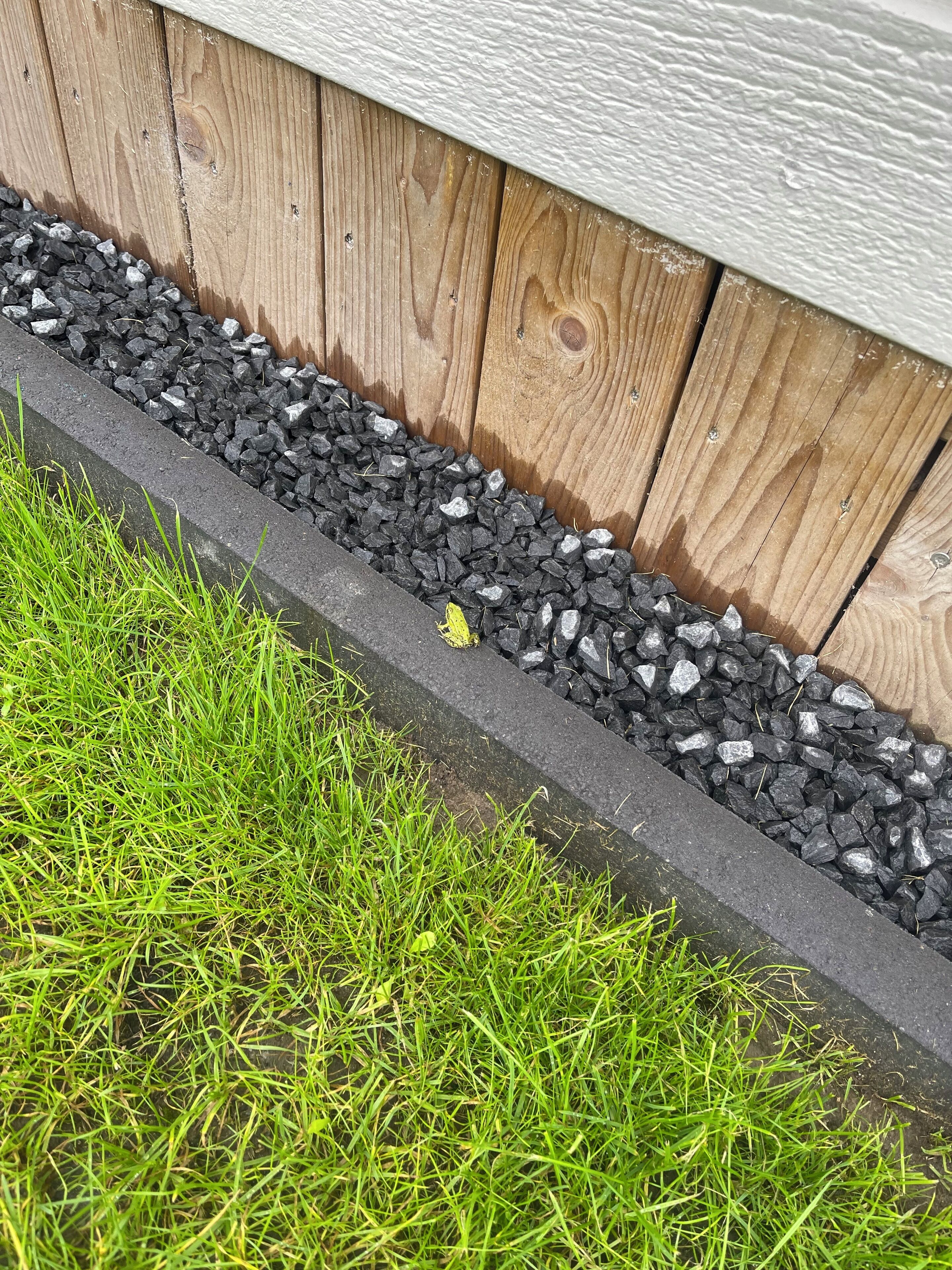 Una jardinera con cerco de madera, camino de grava y césped verde.