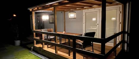 A covered outdoor deck with a wooden railing, a dining table, and chairs.
