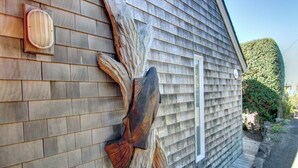 A wooden exterior wall with a large, natural wood carving and a small, rectangular window. - Haystack Haven-Haystack Rock View-Sunset Views-Popular Destination-Unwind (Cannon Beach)