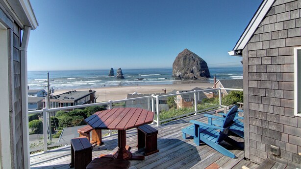 A wooden deck with a table and chairs overlooking a beach with distinctive rock formations. - Haystack Haven-Haystack Rock View-Sunset Views-Popular Destination-Unwind (Cannon Beach)