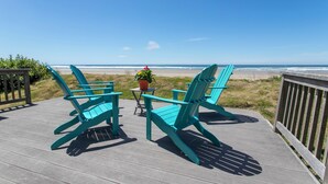 Une terrasse en bois avec des fauteuils Adirondack turquoise et une petite table sur laquelle est posée une plante en pot.
