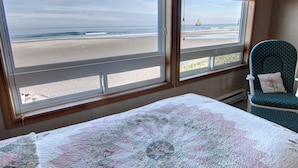 Une chambre avec un lit, une chaise et une vue sur la plage, grâce à de grandes fenêtres.