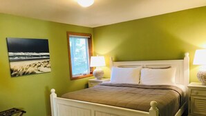 A bedroom with a bed, nightstands, a lamp, a window, and a painting on the wall. - Sea Pines -dog friendly-Spacious and family Friendly-Secluded (Cannon Beach)
