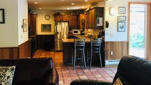 A cozy kitchen with wooden cabinets, a stainless steel refrigerator, and a bar area with two stools. - Sea Pines -dog friendly-Spacious and family Friendly-Secluded (Cannon Beach)