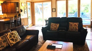 A living room with a black leather sofa, a wooden coffee table, and a kitchen area with wooden cabinets and a bar counter. - Sea Pines -dog friendly-Spacious and family Friendly-Secluded (Cannon Beach)