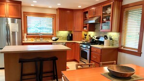 A modern kitchen with wooden cabinets, a stainless steel refrigerator, a gas stove, and a large island with stools. - Koblegarde's Beach House-Unwind and recharge-Fireplace & Cozy Vibes-Peaceful (Cannon Beach)