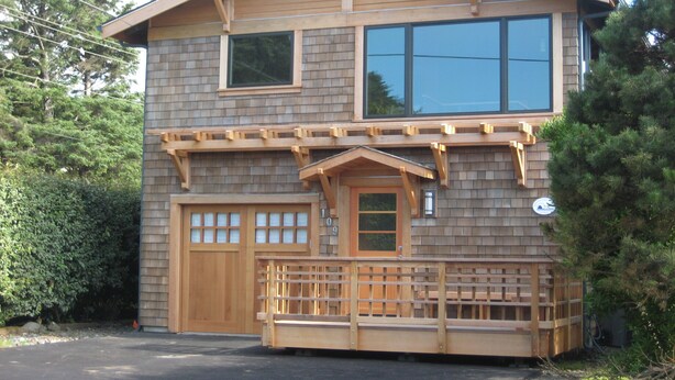 A two-story house with a wooden facade, a front porch with a railing, and a garage with two doors. - Koblegarde's Beach House-Unwind and recharge-Fireplace & Cozy Vibes-Peaceful (Cannon Beach)
