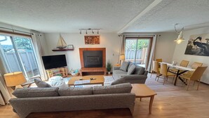 Una sala de estar con sofá, mesa de centro, televisión, chimenea, comedor y ventanas amplias.