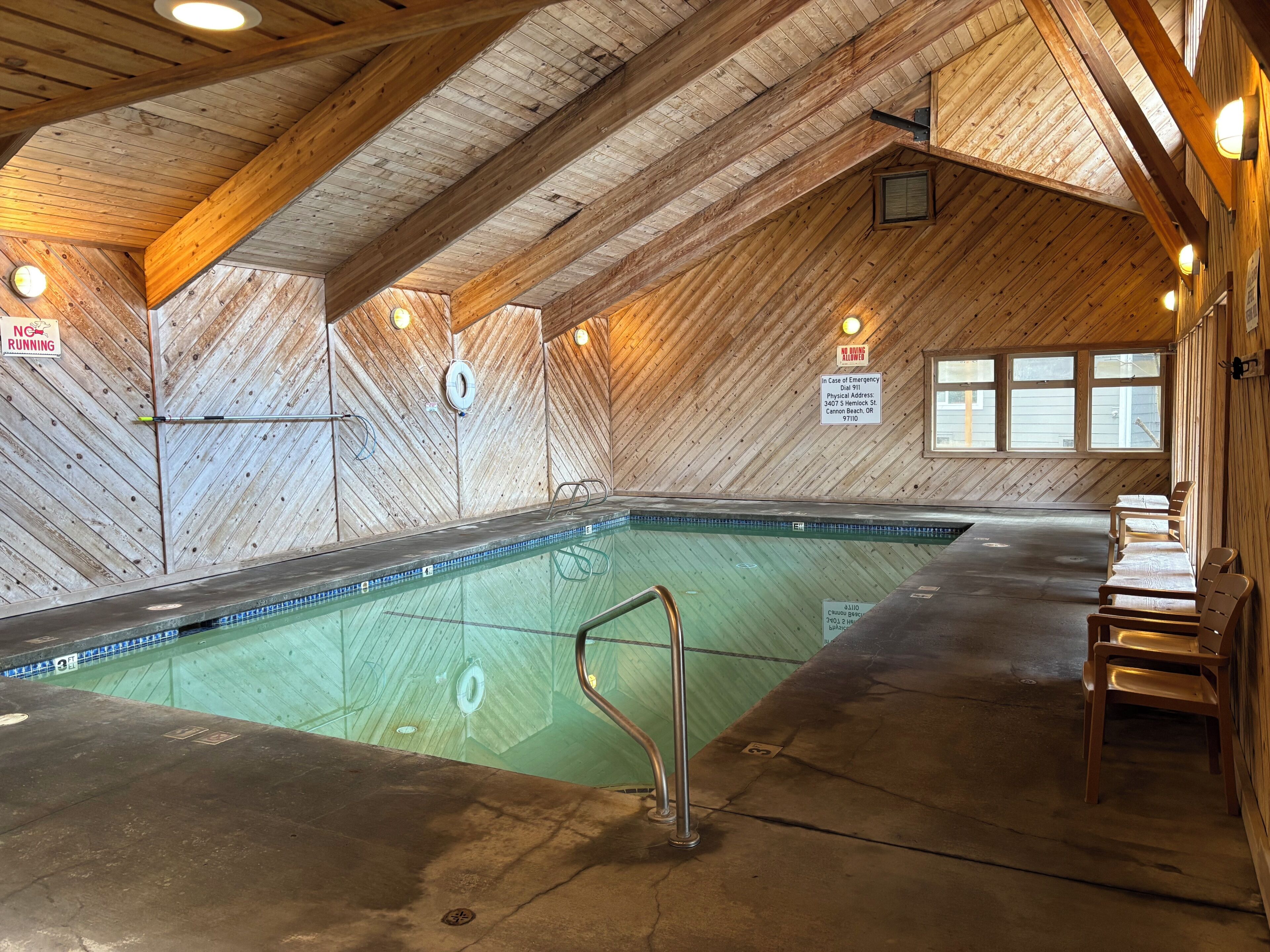 Une piscine intérieure avec des murs et un plafond en bois, des bancs le long des côtés et les coordonnées des personnes à contacter en cas d’urgence affichées sur le mur.