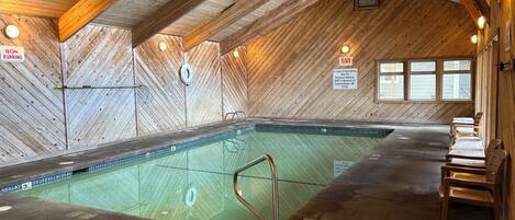 Une piscine intérieure avec des murs et un plafond en bois, des bancs le long des côtés et les coordonnées des personnes à contacter en cas d’urgence affichées sur le mur.