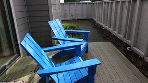 Dos sillas Adirondack azules en una terraza de madera con una valla blanca al fondo.