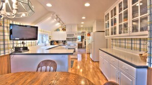 A modern kitchen with white cabinetry, a wooden dining table, and a built-in TV.