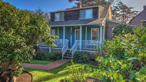 A two-story house with a front porch, a brick pathway, and a well-maintained garden.