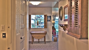 A hallway with a wooden bench, a window with shutters, and a door leading to another room.