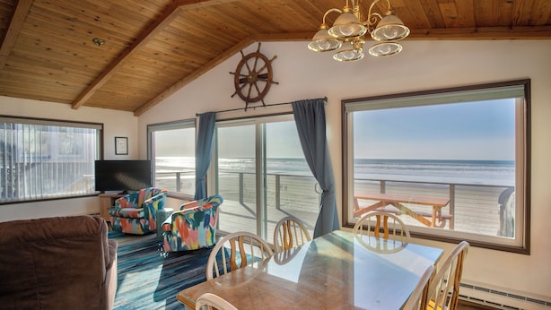 Una stanza con soffitto in legno, un'ampia finestra vista mare, un tavolo da pranzo con sedie, un divano e una televisione.