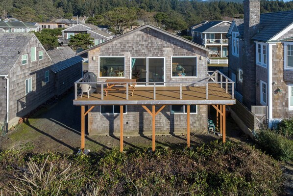Une maison dotée d’une terrasse en bois, de grandes fenêtres et d’un balcon.