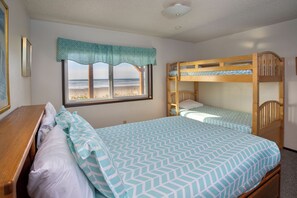 Une chambre avec un lit superposé, un lit simple, une fenêtre donnant sur la plage et un bureau en bois.