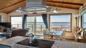 Una cucina con un fornello, un'area pranzo con sedie e un tavolo, e ampie finestre vista spiaggia.