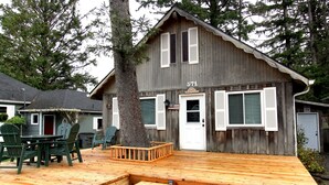 Une cabane en bois dotée d’une terrasse, d’un coin repas avec des chaises et d’une boîte aux lettres.