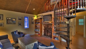 Un salon chaleureux avec une cheminée, des étagères à livres, un escalier et un téléviseur.