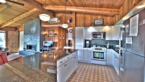 A modern kitchen with granite countertops, stainless steel appliances, and a brick fireplace. - Sand Pads - Ocean View- Sunset Views-Guest Favorite-Ideal For Families- (Cannon Beach)