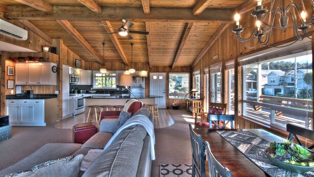 A spacious living area with a sofa, a dining table with chairs, and a kitchen in the background. - Sand Pads - Ocean View- Sunset Views-Guest Favorite-Ideal For Families- (Cannon Beach)