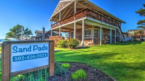 A two-story house with a covered porch and a sign in front. - Sand Pads - Ocean View- Sunset Views-Guest Favorite-Ideal For Families- (Cannon Beach)