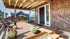 A wooden deck with outdoor seating, a door with a number, and a building in the background. - Sand Pads - Ocean View- Sunset Views-Guest Favorite-Ideal For Families- (Cannon Beach)
