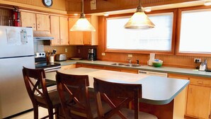 Cucina con mobili in legno, frigorifero, piano cottura, lavello e due lampade a sospensione.